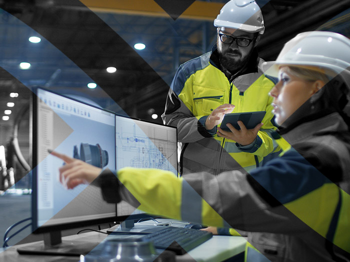 Image showing two warehouse workers wearing high visibility jackets and hard hats discuss load shifting at computer.